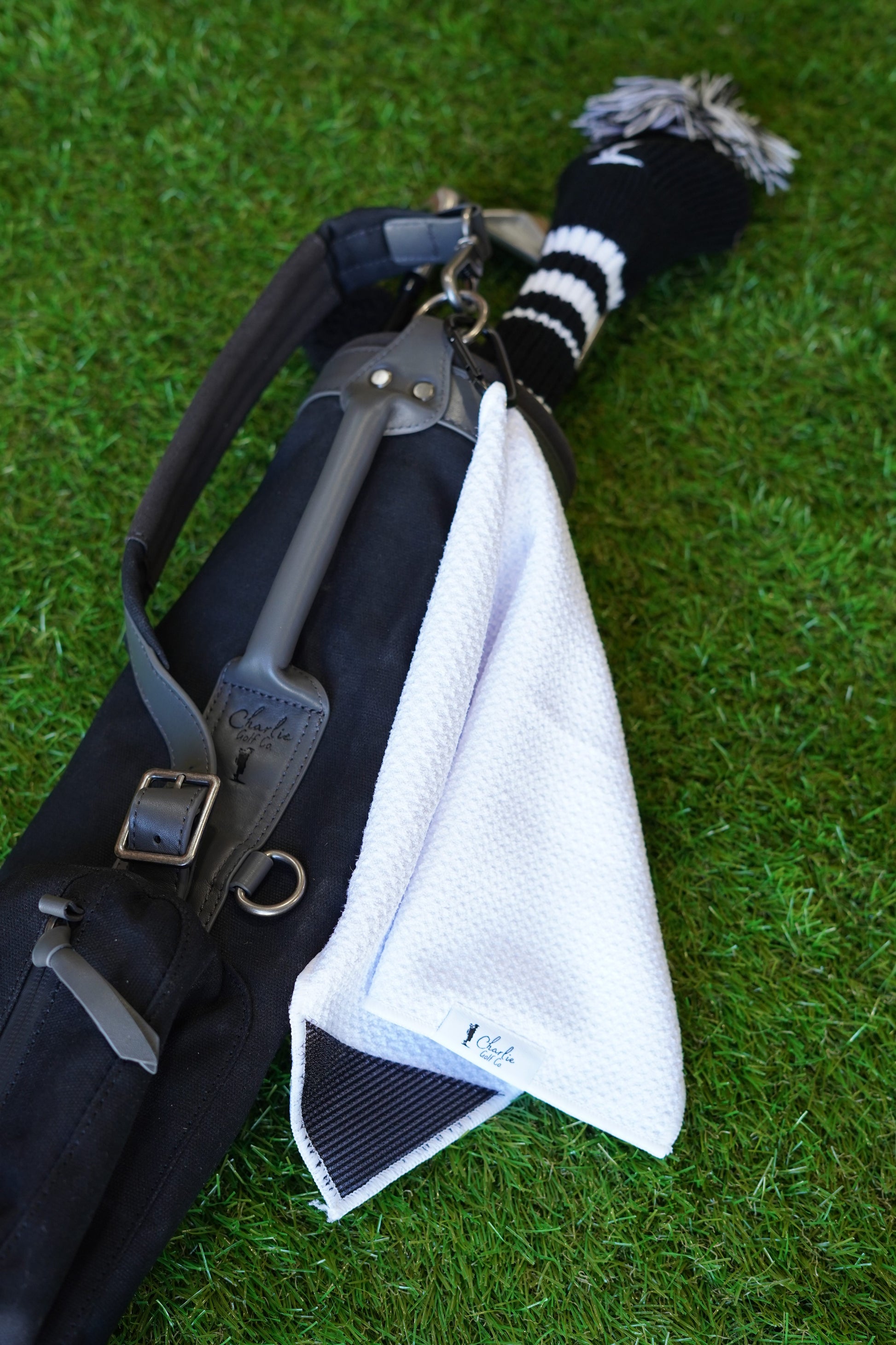 Kids golf bag with a white towel and black and white striped golf club head cover on grass